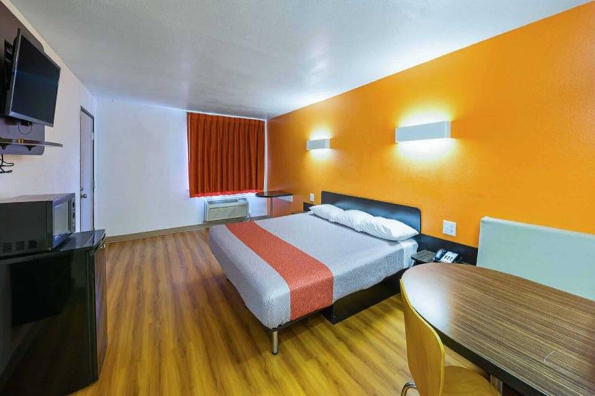 Een hotelkamer met een bed, een bureau, een televisie en een raam met gordijnen.