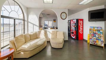 Un intérieur moderne comprenant un canapé, des fauteuils, une horloge, un distributeur automatique et un téléviseur.