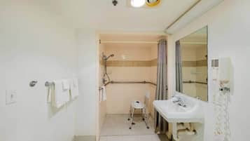 Een badkamer met een witte wastafel, een spiegel, een douchegedeelte en een rolstoel.