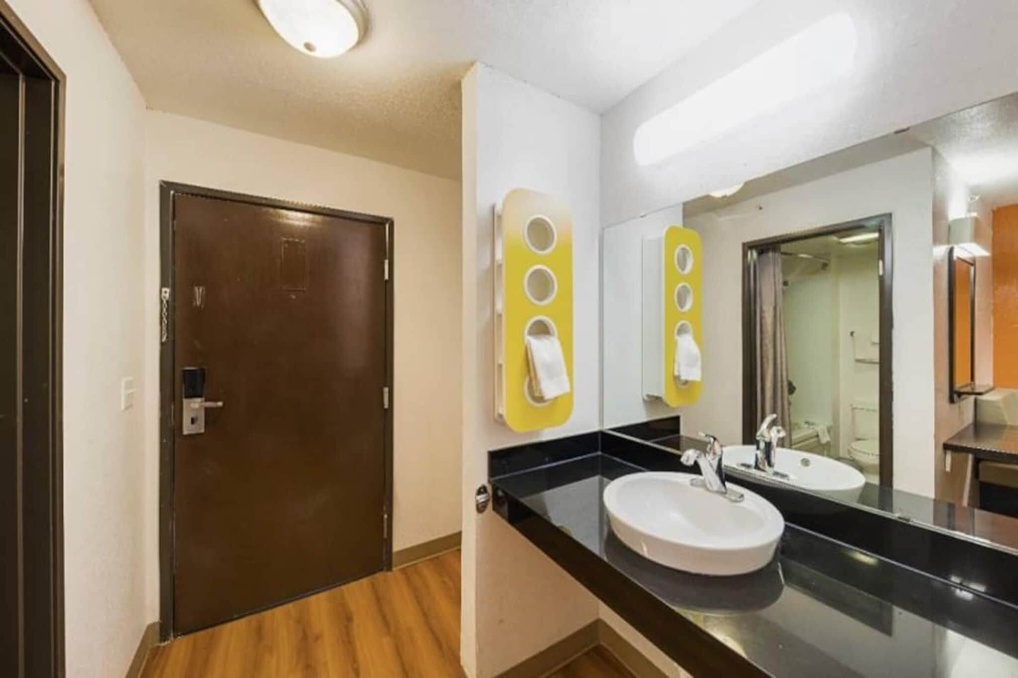 A hotel bathroom with a wooden door, a sink with a mirror, and a towel dispenser.