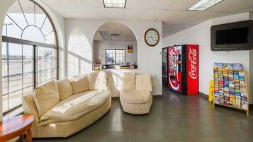 A modern interior with a sofa, armchairs, a Coca-Cola vending machine, and a television.