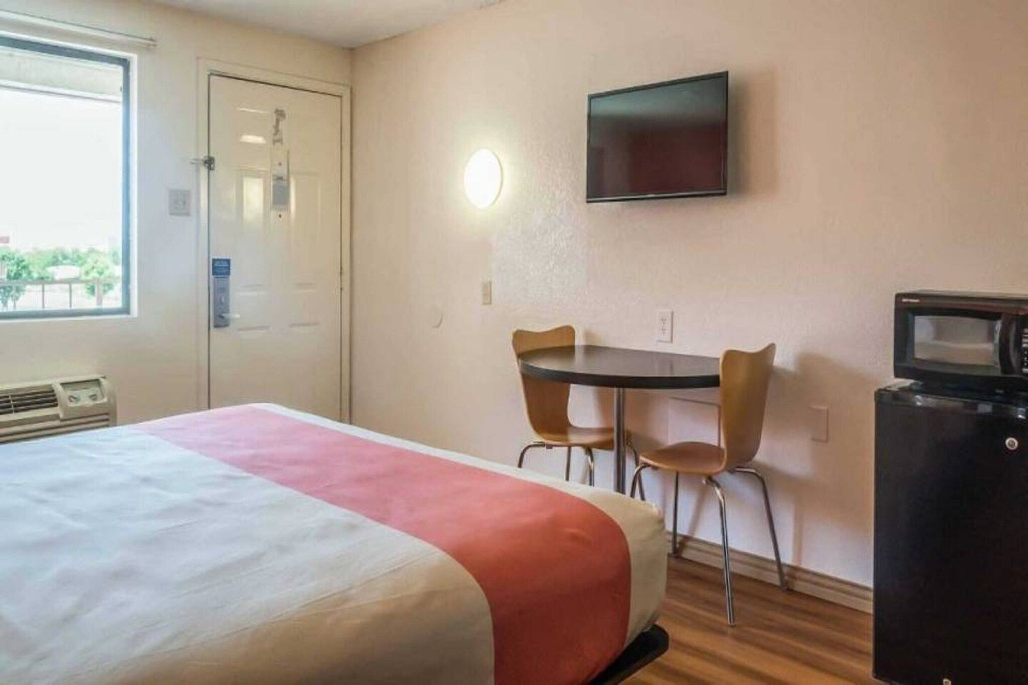 A hotel room with a bed, a desk, two chairs, a television, and a microwave.