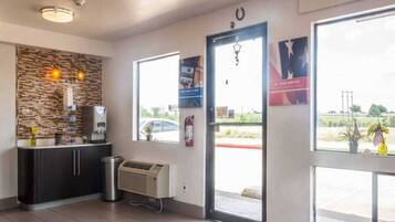 A reception area with a stone wall, a counter with a coffee machine, a trash can, and a fire extinguisher.