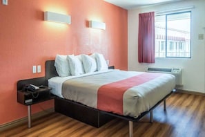 Habitació d'hotel amb un llit, una tauleta de nit i una finestra amb cortines.