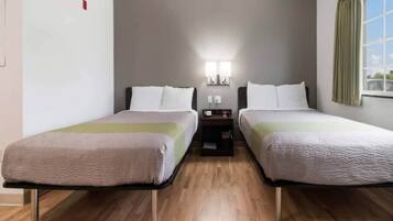 A hotel room with two beds, a nightstand, a lamp, and a window with curtains.