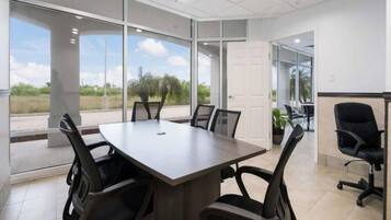 A conference room with a large table and chairs, large windows, and a view of the outdoors.