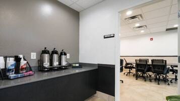A reception desk with coffee dispensers, a sign indicating a conference room, and office chairs in the background.