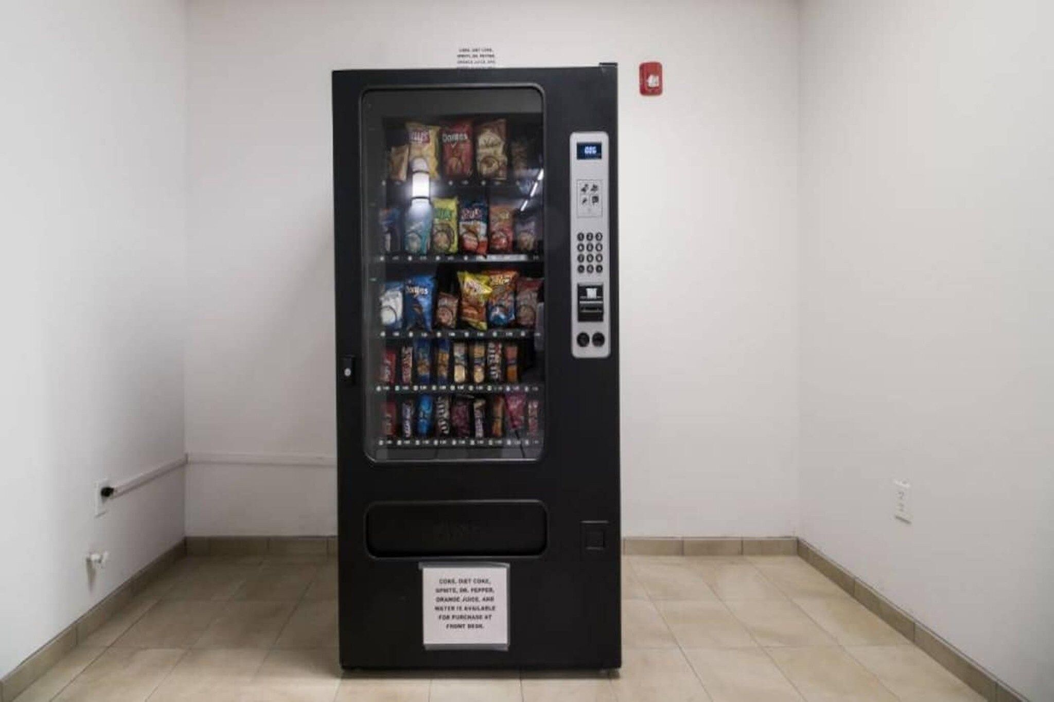 A vending machine with a variety of snacks and drinks, a keypad, and a sign indicating the availability of water for purchase.