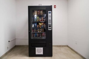 Een automaat met diverse snacks en dranken, een keypad en een bordje waarop staat dat water te koop is.