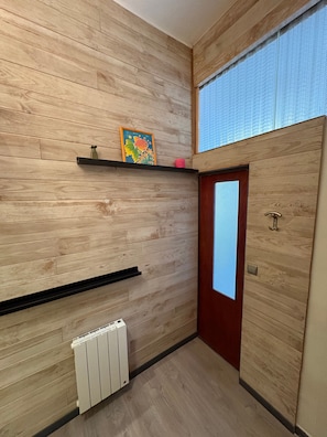 Un couloir aux murs recouverts de lambris en bois, un radiateur, une porte avec une fenêtre et une étagère sur laquelle est posée une photo encadrée.