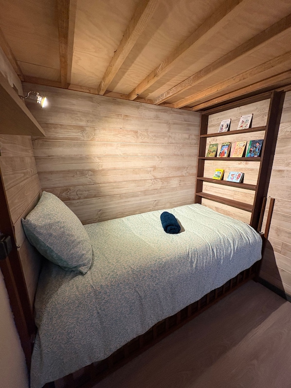Un lit simple avec une couvre-lit à motifs, dans une pièce aux murs en bois et au plafond en pente.