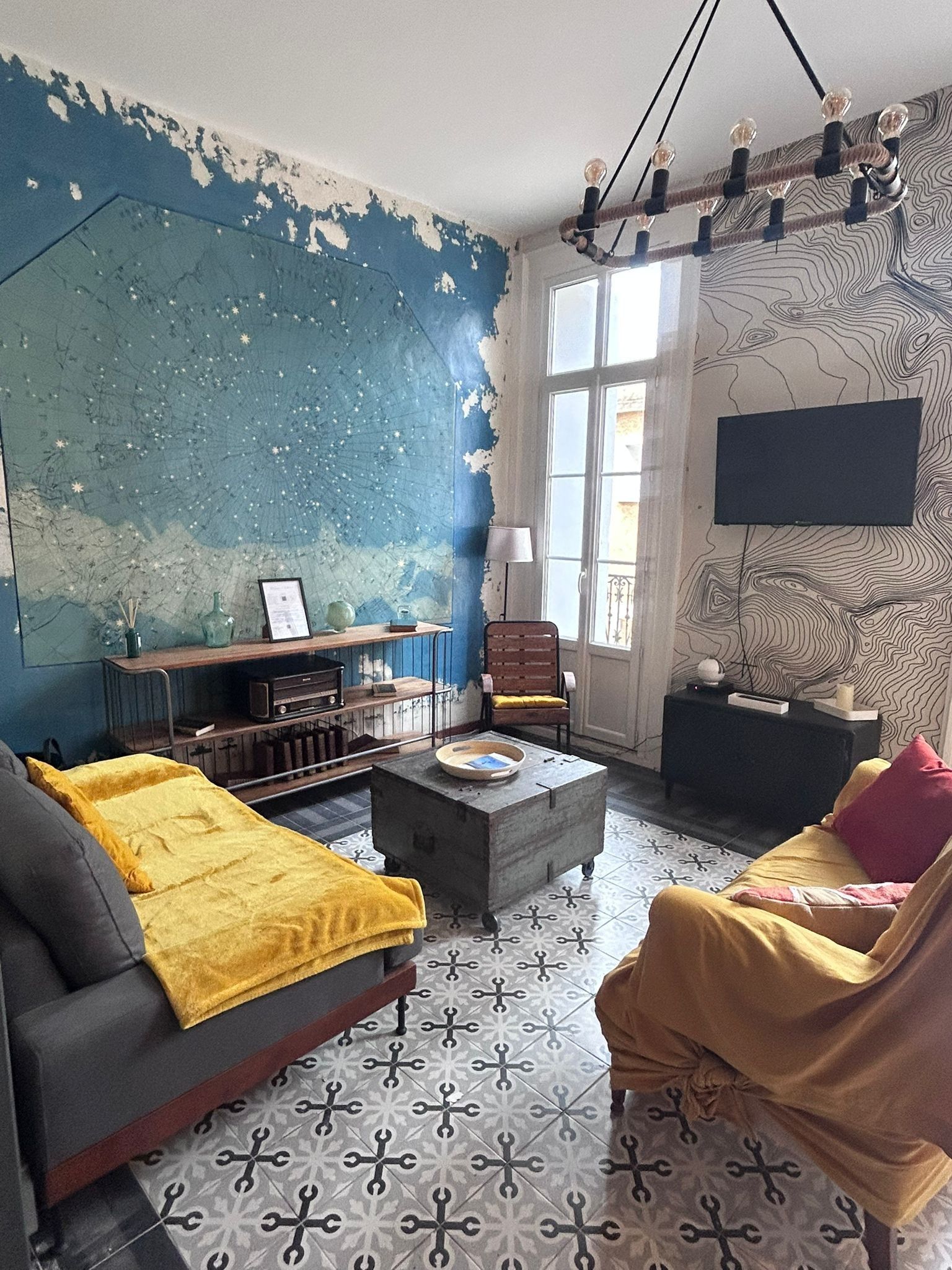 Een woonkamer met een blauwe muur, een vloer met patroon, een bank, een fauteuil, een salontafel en een flatscreen-televisie die aan de muur is bevestigd.