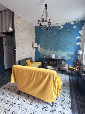 Une pièce avec un lit recouvert d’un tissu jaune, un bureau avec un ordinateur, une chaise et un mur décoré d’une carte.