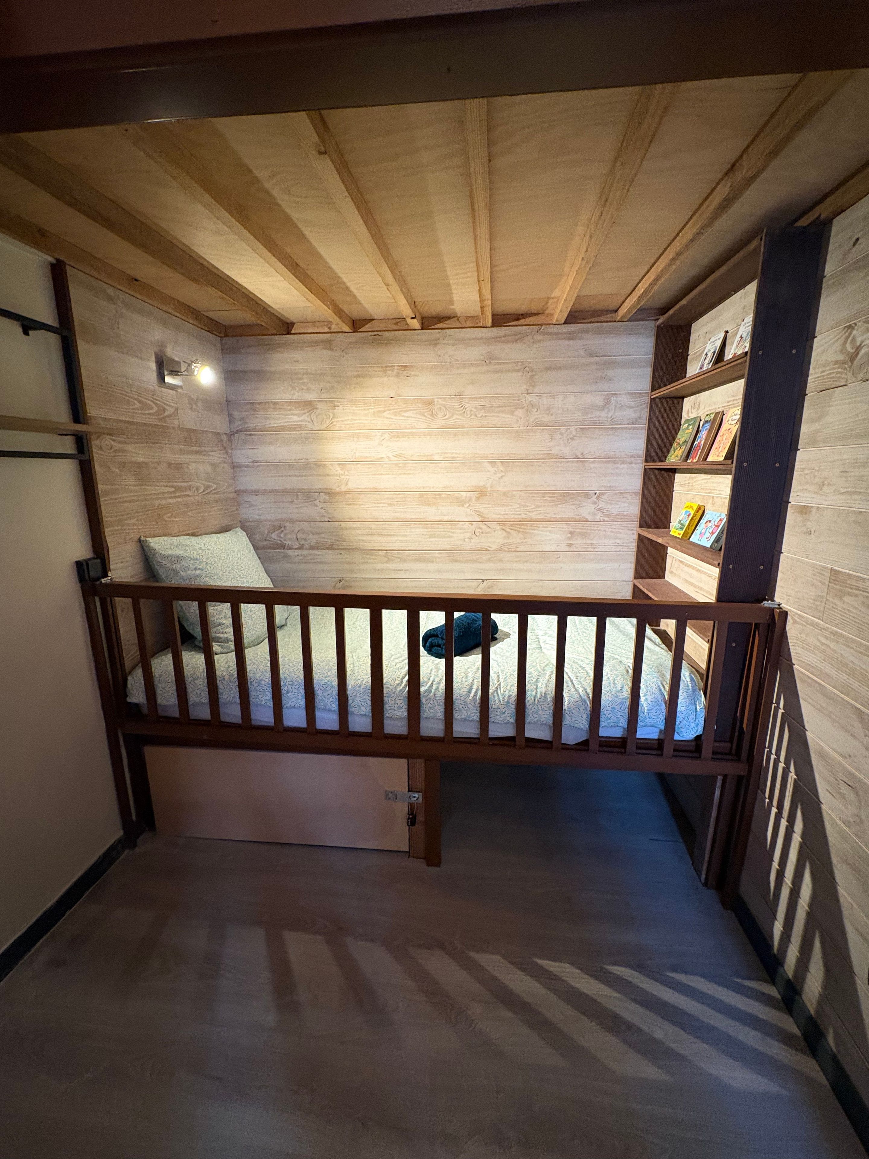 Een kleine kamer met een houten stapelbed, een bureau en een boekenplank.