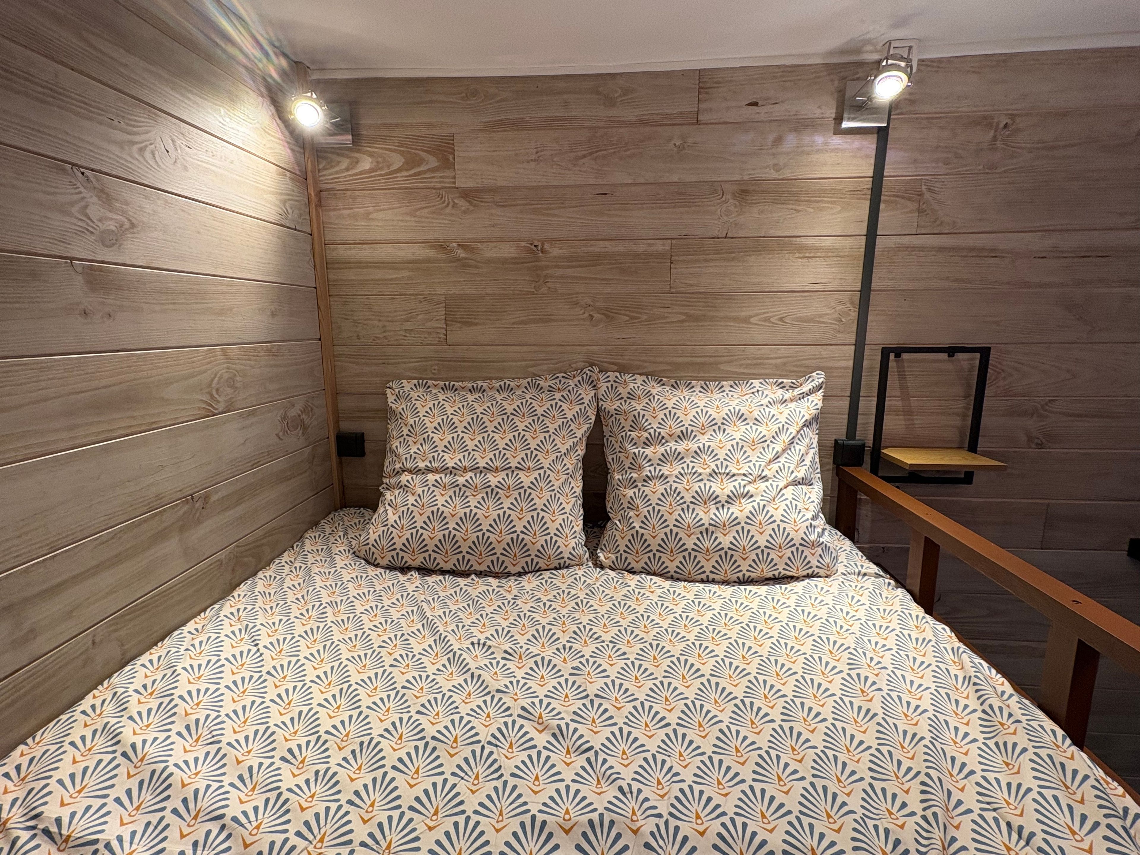 Ein Zimmer mit Holzwandverkleidung, einem Bett mit gemusterten Bettwaren und einem Nachttisch mit Lampe.