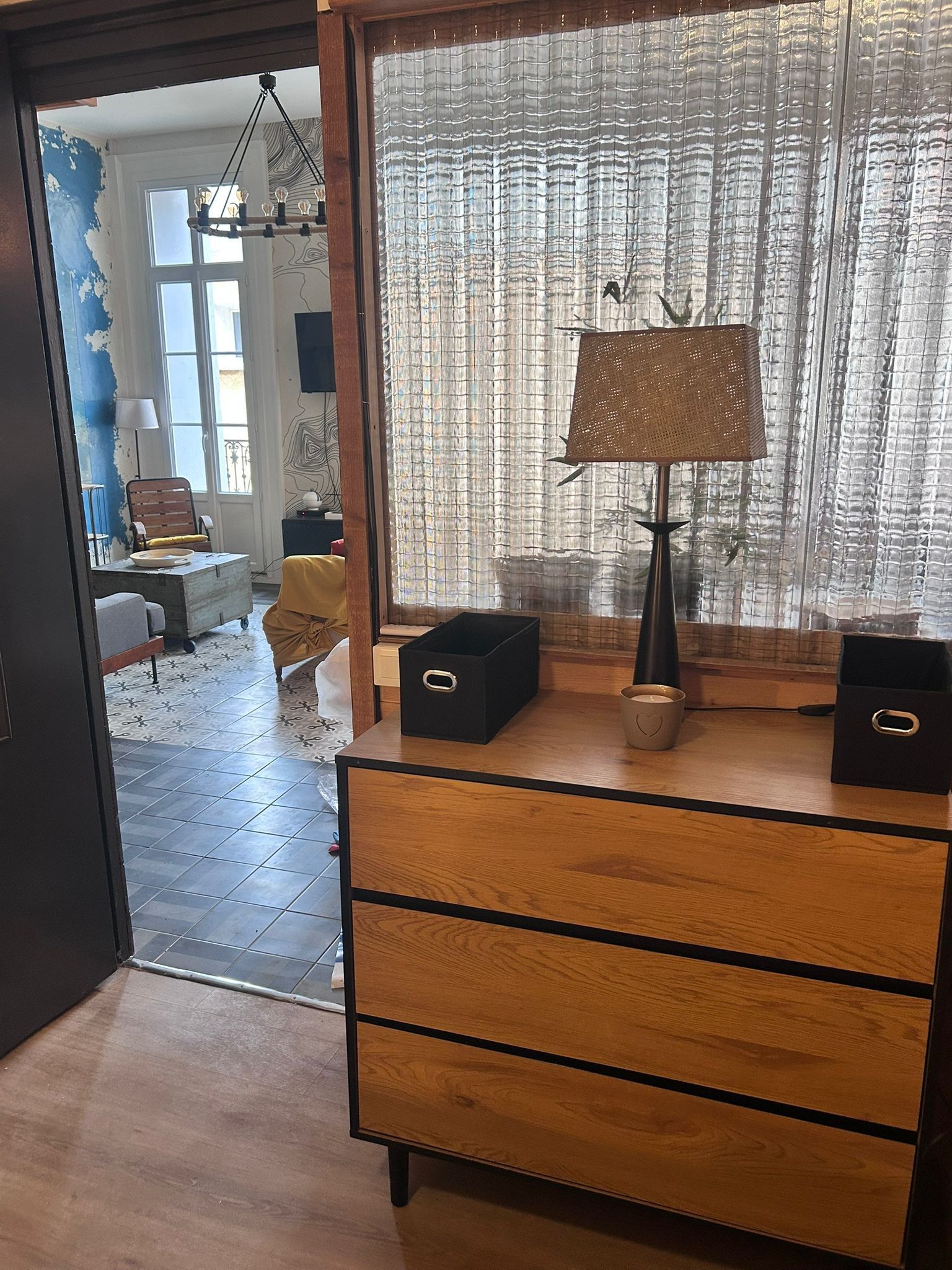 Ein Zimmer mit einem Holzkapuzenkleid, einer Lampe und einem Fenster mit gemusterten Vorhängen.