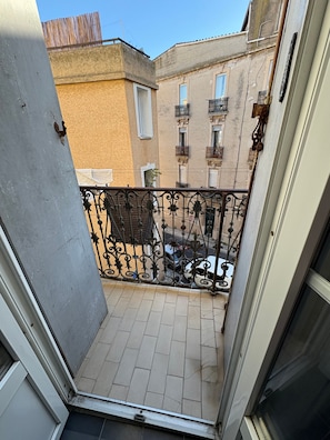 Un balcon doté d’une rambarde en métal, d’un sol carrelé et offrant une vue sur les bâtiments voisins.