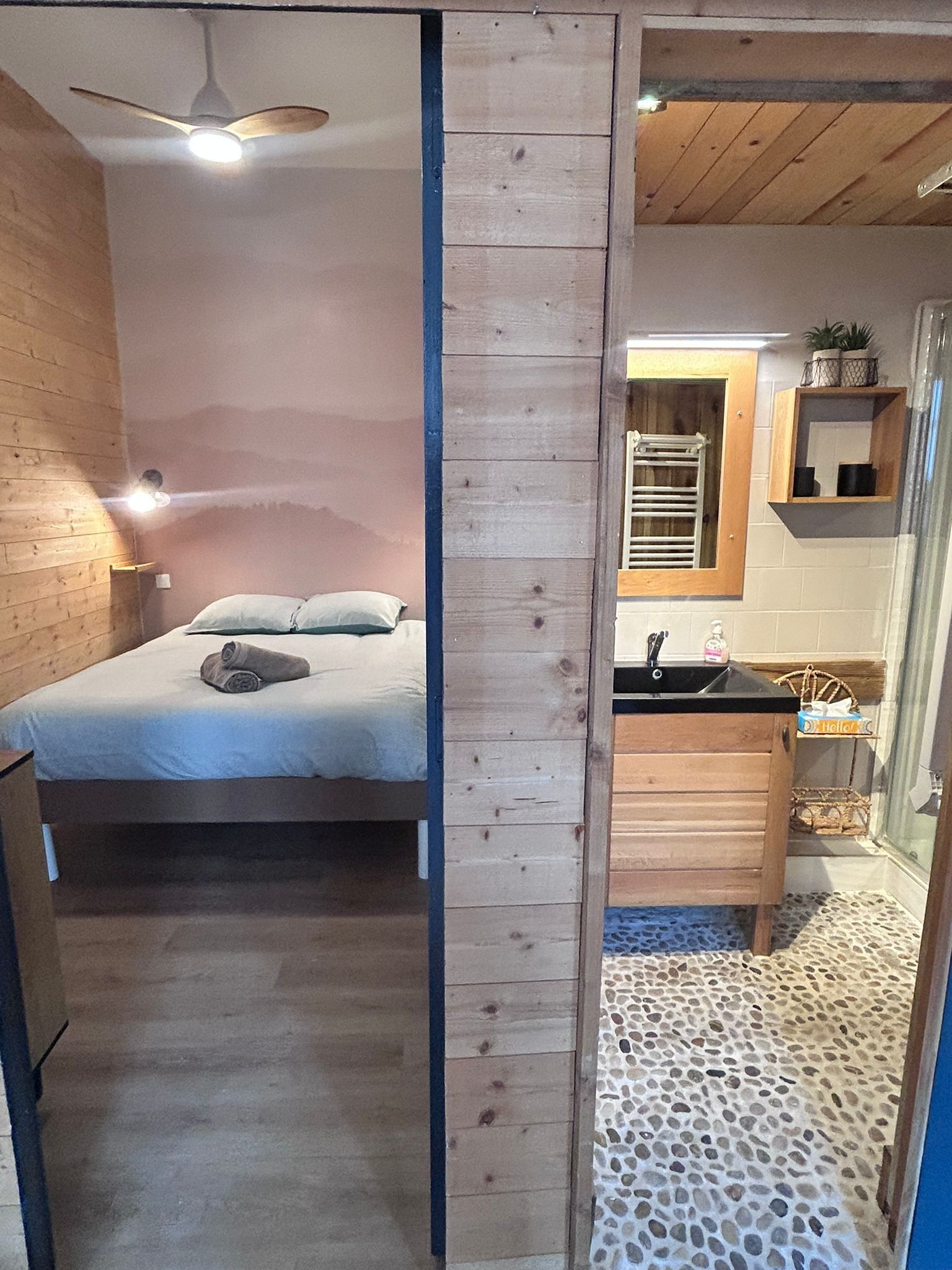 Een slaapkamer met een bed, een plafondventilator en een nachtkastje.