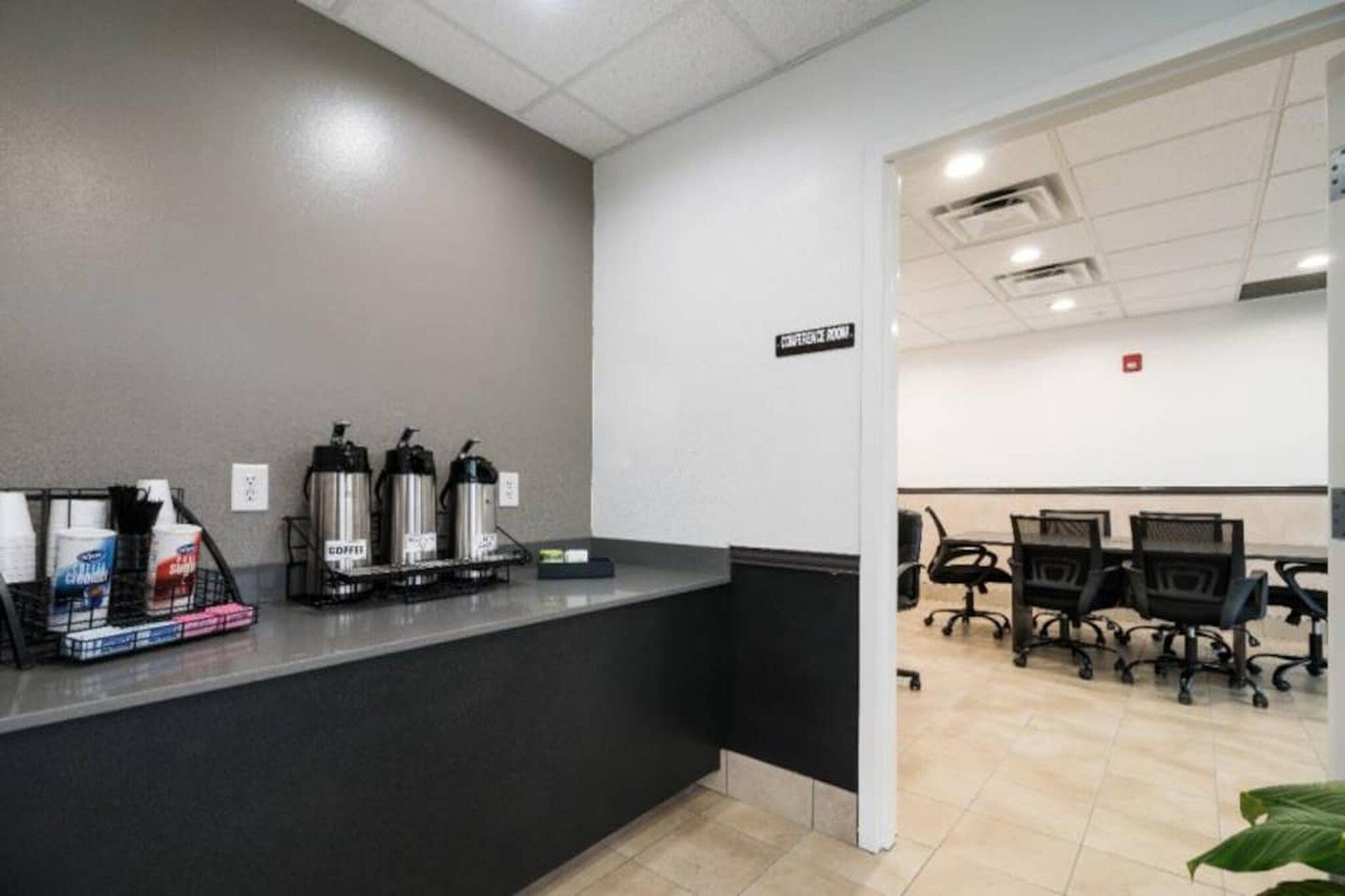 A reception area with a coffee station, a sign indicating a conference room, and office chairs in the background.