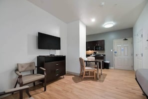 A compact living space with a flat-screen TV mounted on the wall, a dining area with a table and chairs, and a kitchenette in the background. - Cozy 1 Queen Bed | Nsmk, Kitchen (INGLESIDE)