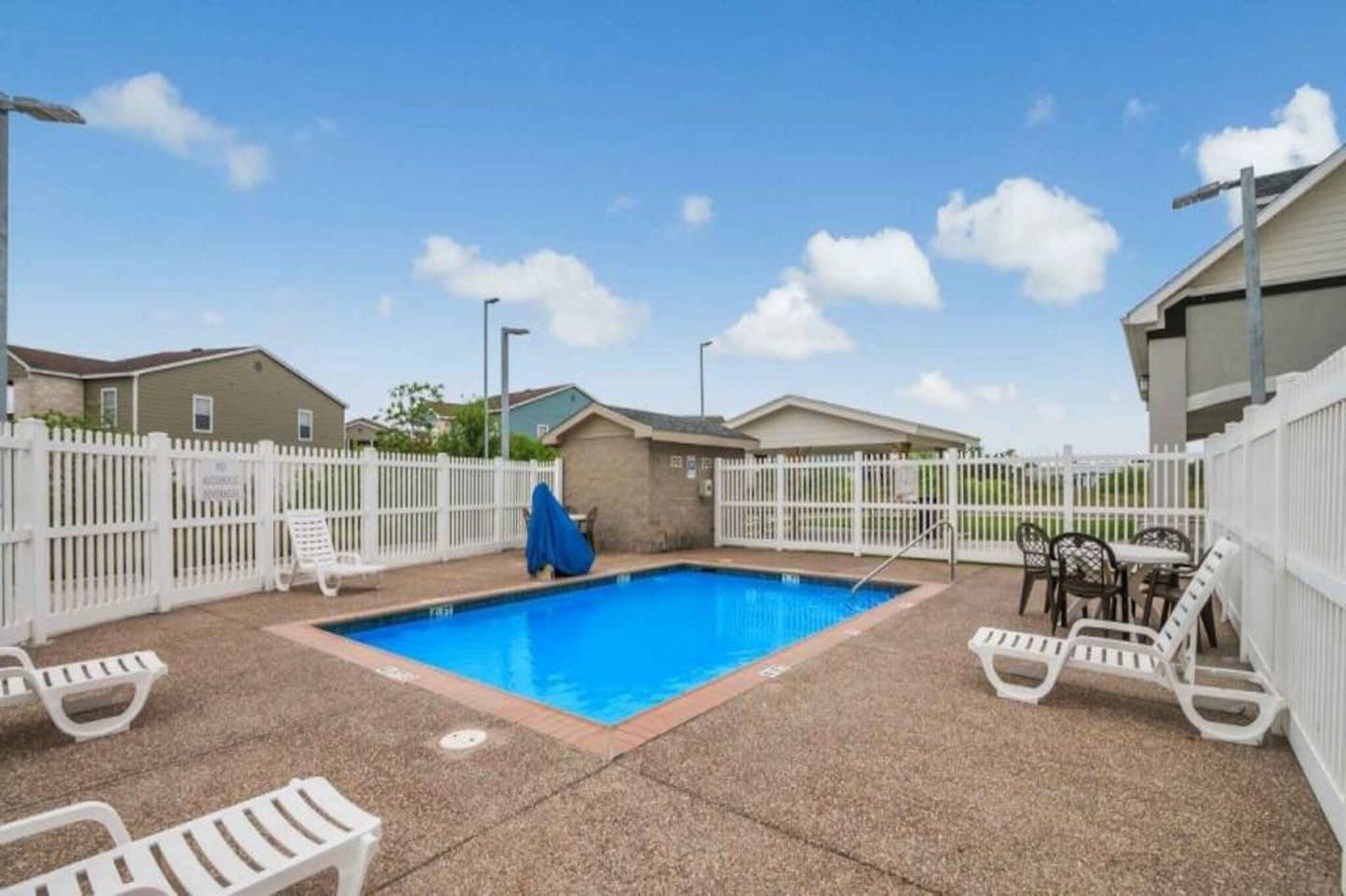 A swimming pool with a white fence, lounge chairs, and a covered seating area.