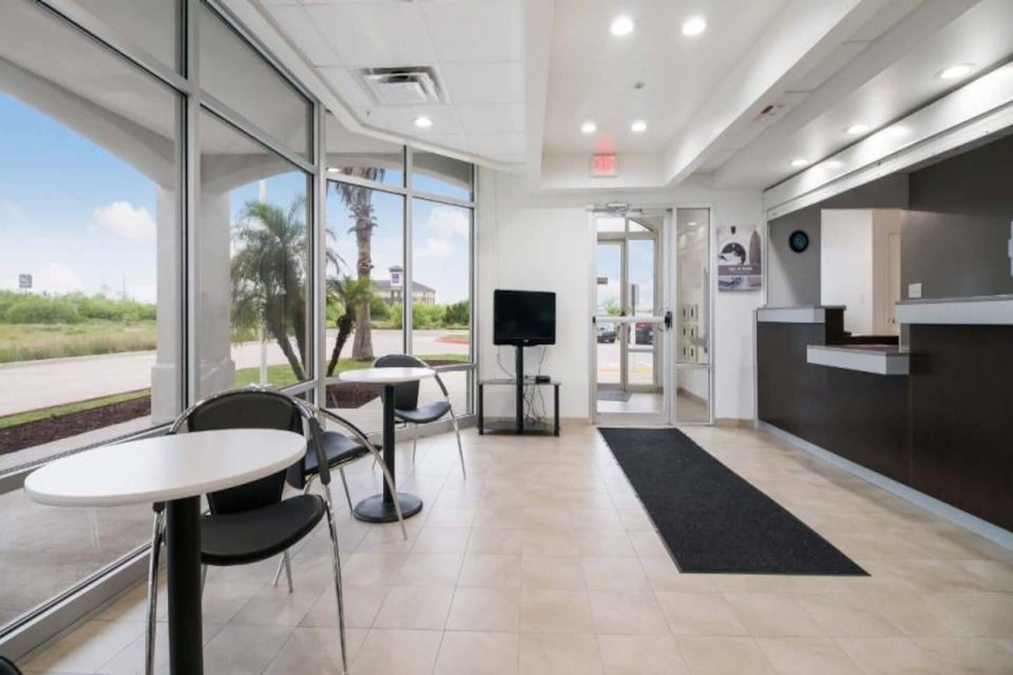 A modern indoor space with a reception desk, a TV, and seating area with tables and chairs.
