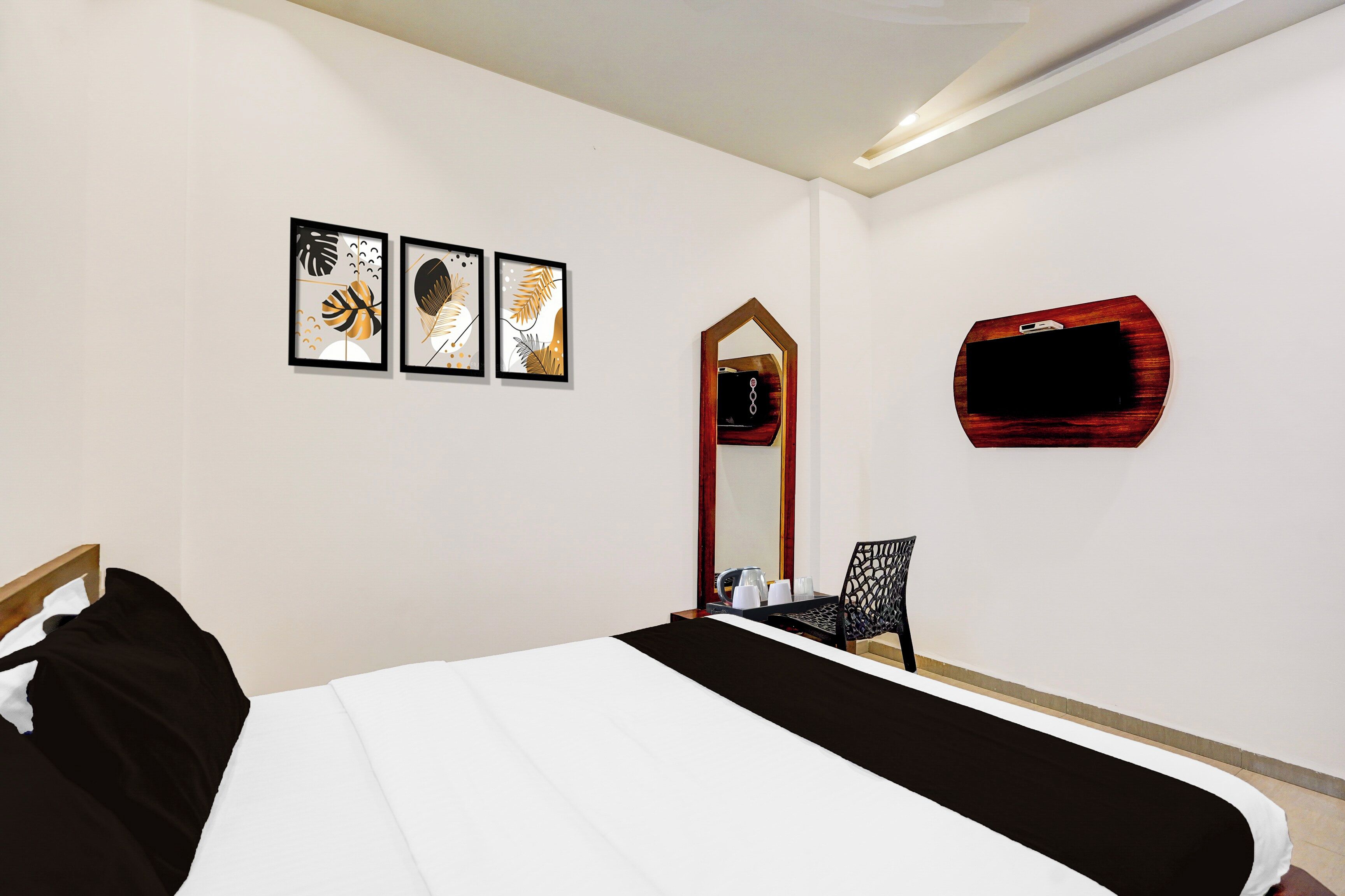 Habitación de hotel con cama, una silla, un espejo y tres cuadros enmarcados en la pared.
