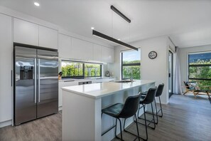 A modern kitchen with a large island, stainless steel appliances, and a view of greenery outside. - Waterways No. 6 - Whitianga (Whitianga)