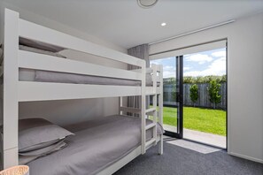 A bunk bed room with a sliding glass door leading to a grassy outdoor area. - Waterways No. 6 - Whitianga (Whitianga)