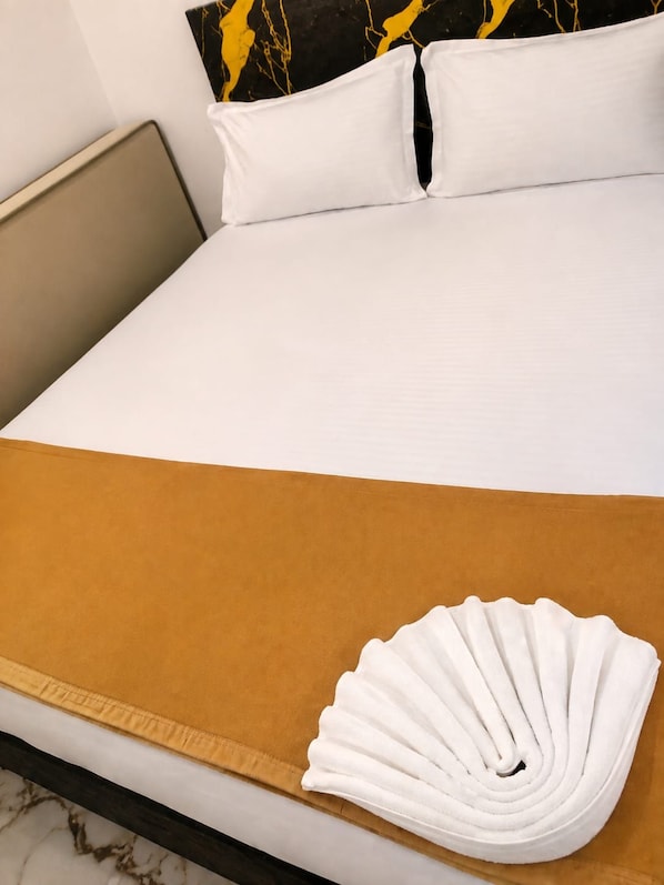 A neatly made bed with a white pillow and a folded white towel.