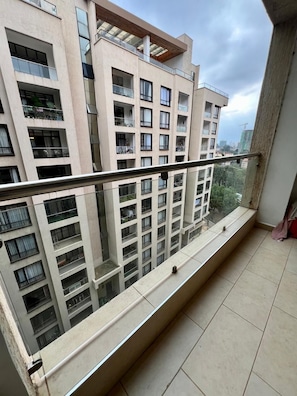Een balkon met een metalen hekwerk, met uitzicht op een woongebouw met meerdere balkons en ramen.