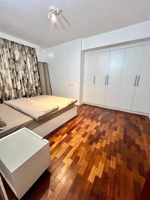 A bedroom with a bed, a wardrobe, and a wooden floor. - Finewood Residency View Palace Apartment (Nairobi)