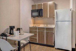 A compact kitchen with a microwave, refrigerator, and a small dining table with chairs. - 1 King Bed | Suite, Non-Smoking (Dallas)