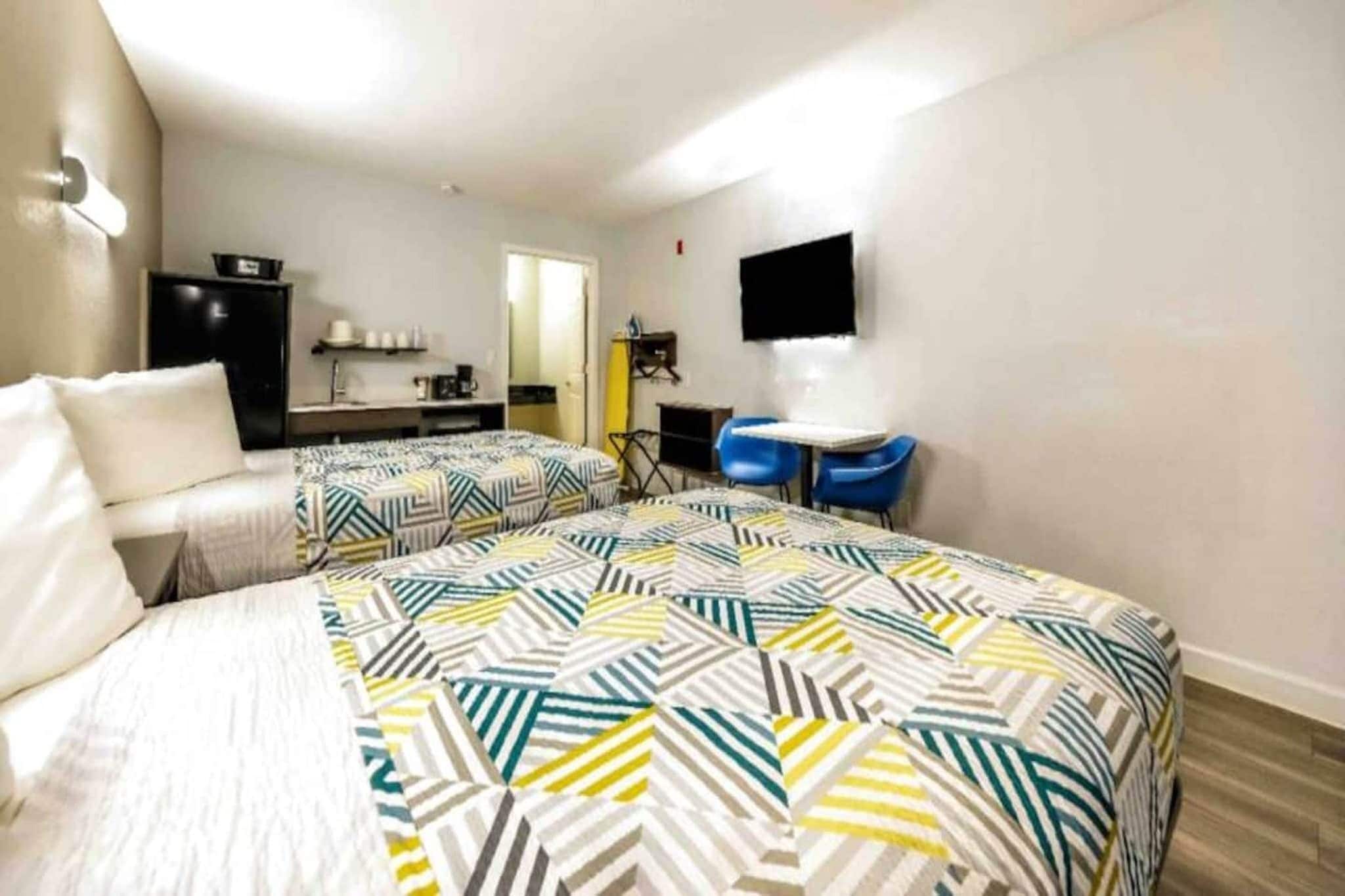 Ein Hotelzimmer mit zwei Betten, einem Schreibtisch, einem Stuhl, einem Fernseher und einem kleinen Tisch.