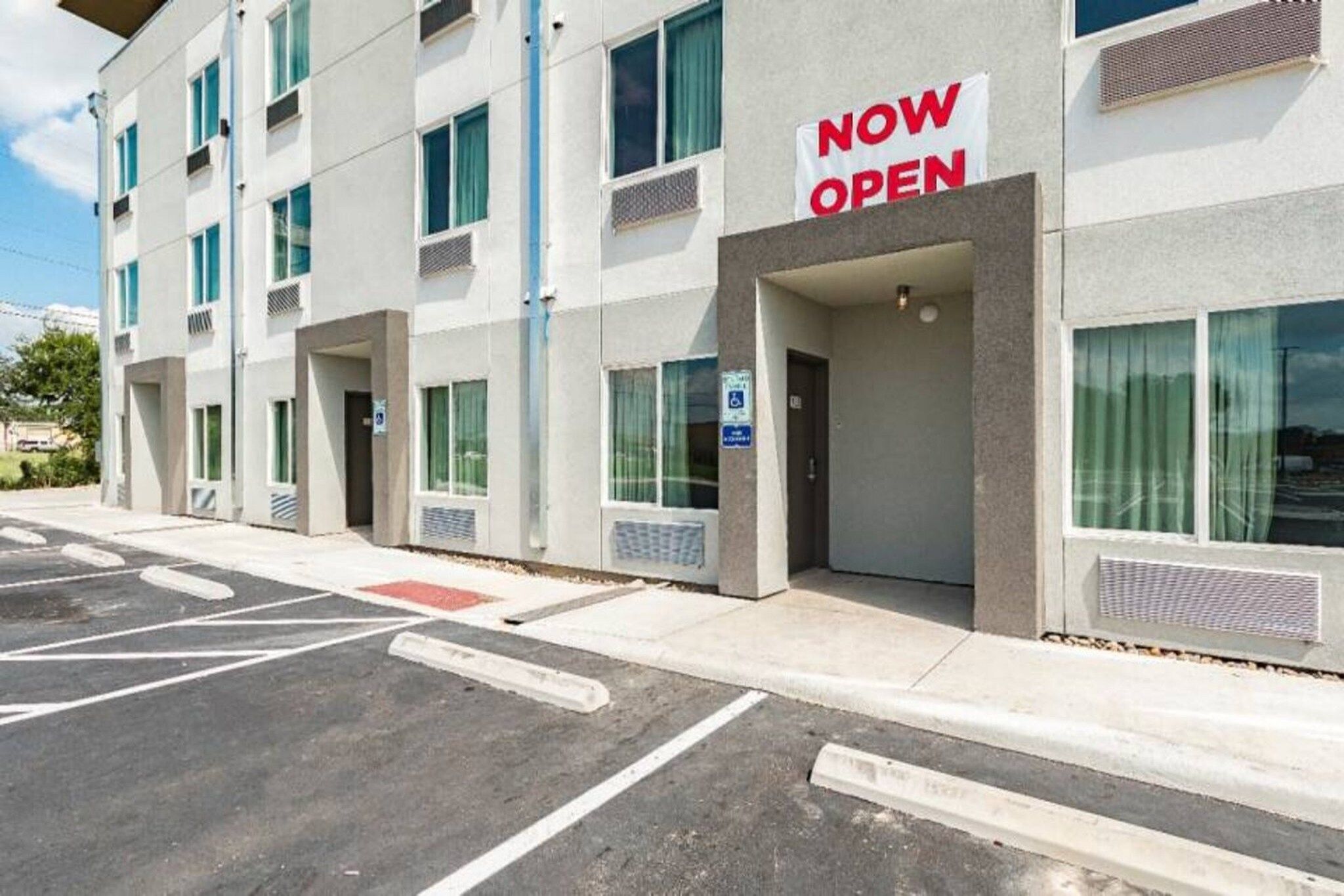 A building with a 'NOW OPEN' sign, a parking lot, and a wheelchair-accessible entrance.
