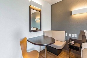Une chambre d’hôtel moderne avec une table ronde, deux chaises, un canapé, une table de chevet avec une lampe et un miroir au mur.