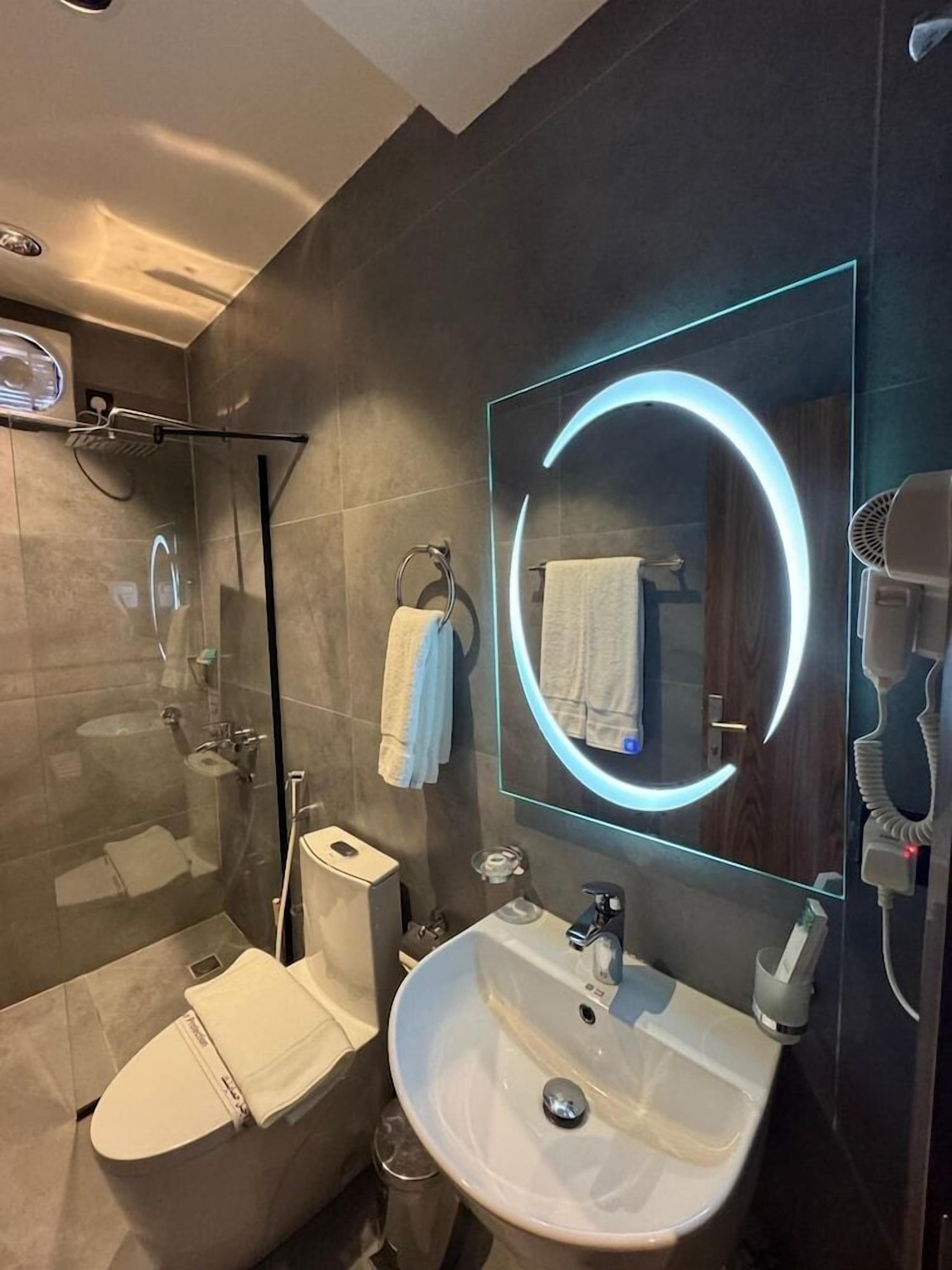 A modern bathroom with a glass-enclosed shower, a white sink, and a mirror with a circular light.