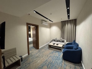 Hotellihuone, jossa on sänky, oleskelualue sohvineen ja nojatuoleineen, televisio ja pieni pöytä.