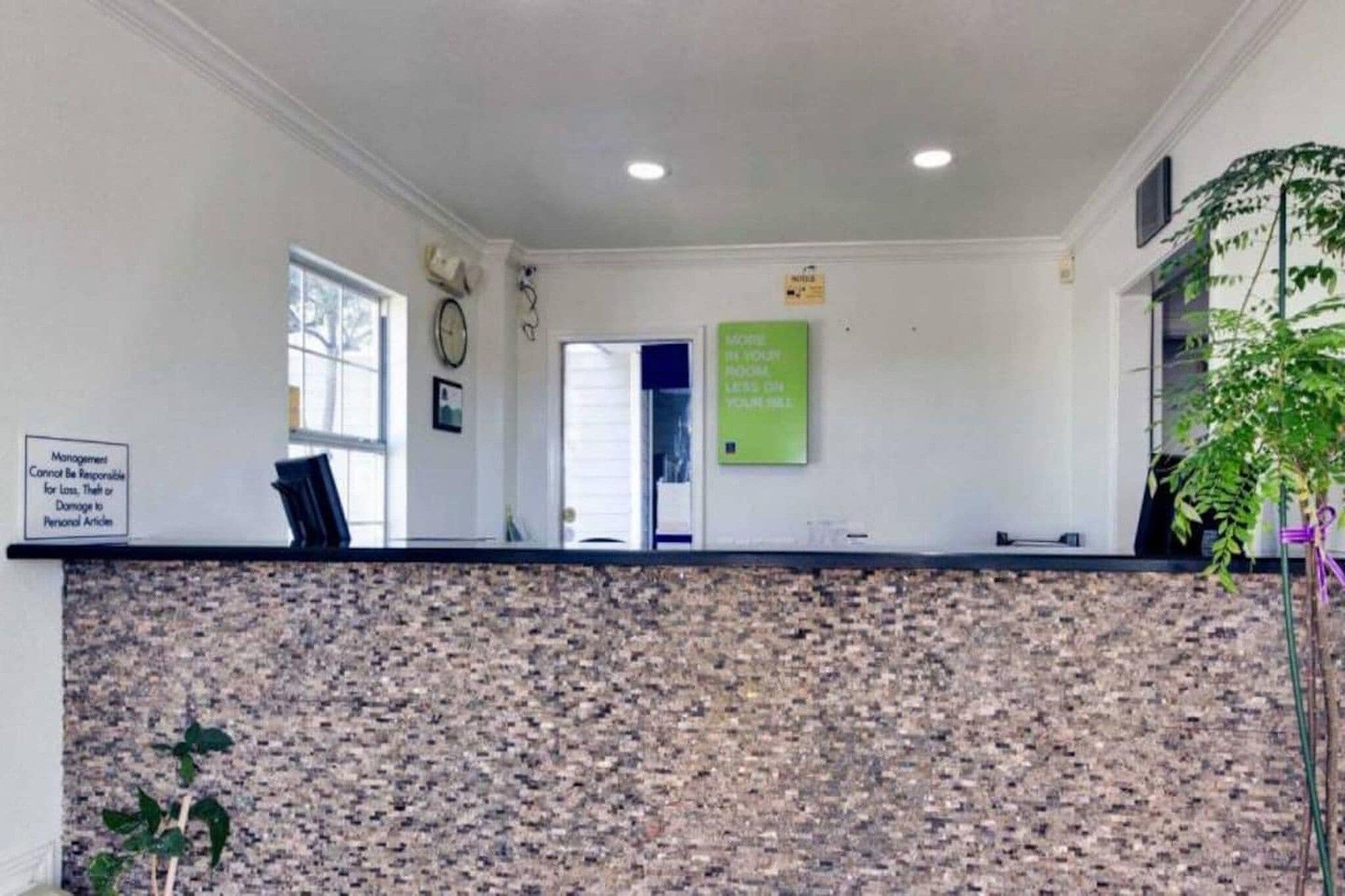 A reception area with a stone wall, a clock, a sign about room rates, and a plant.