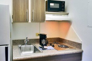 A compact kitchenette with a stainless steel sink, a coffee maker, a microwave, and a gas stove. - Spacious 1 Queen Bed | ADA/Tub, Nsmk (Dallas)