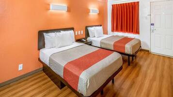 A hotel room with two beds, wooden flooring, and a red curtain.