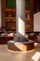 Uma área de bar moderna com disposição circular de assentos, prateleiras de madeira com garrafas e um grande pilar.
