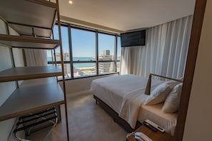 Quarto de hotel com cama, escrivaninha, televisão e vista para a praia e oceano.
