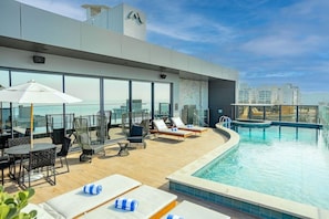 A rooftop pool area with lounge chairs, umbrellas, and a view of the city skyline. - Brava Mundo Boutique Hotel (Itajai)