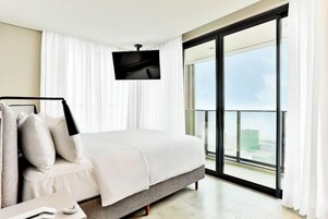 Quarto de hotel moderno com cama grande, televisão de tela plana na parede e varanda com vista para a cidade.