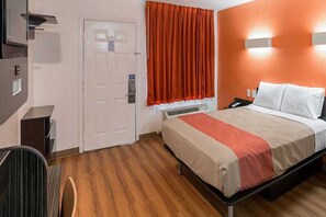 Habitación de hotel con cama, escritorio, silla, puerta y ventana con cortinas.