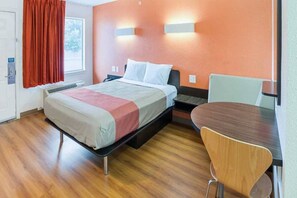 A hotel room with a bed, bedside table, chair, and a window with curtains. - Cozy QUEEN BED | MOB ACC TUB NSMK (GRAND PRAIRIE)