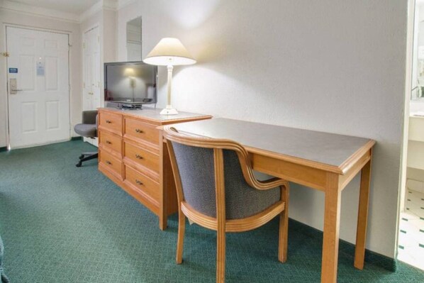 Una camera d'albergo con una scrivania in legno, una sedia, un televisore su un comò e una lampada.
