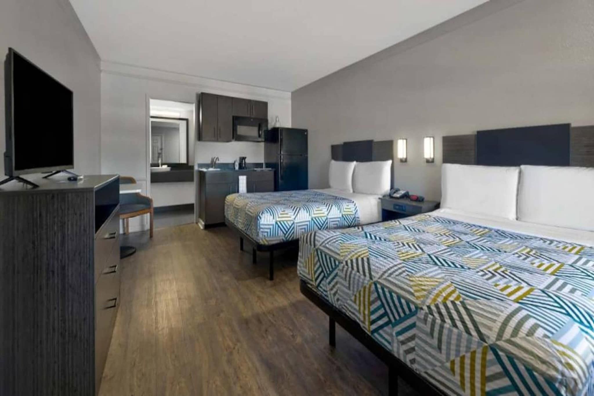 A hotel room with a bed, a desk, a chair, a TV, a kitchenette, and a bathroom.