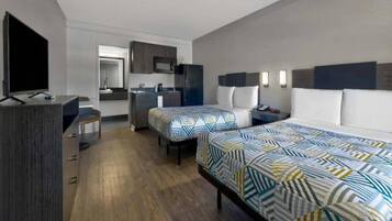 A hotel room with a bed, a desk, a chair, a TV, a kitchenette, and a bathroom.